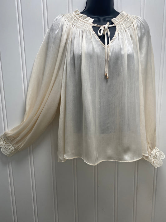 An off-white/cream sheer long-sleeve blouse with lace trim and a tie-neck detail, displayed on a black mannequin torso against a white paneled wall. 